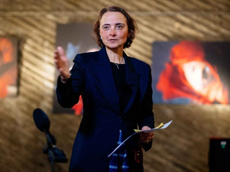 Seona Sommer fotografiert von Costa Belibasakis Seona Sommer eröffnet eine Kunstausstelluing und steht dabei vor einer Wand mit Kunstwerken.